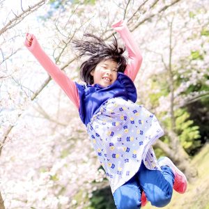 娘が満開の桜の下で、元気にジャンプしている様子です。