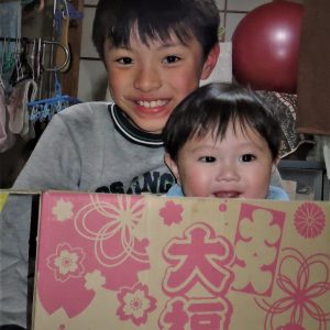 私の長男と次男の孫の二人です。幸せを願って、「大入り大福箱」に小さい次男の孫が入って2人を撮影。小さい孫はママの方を見て、やっと笑ってくれました。
